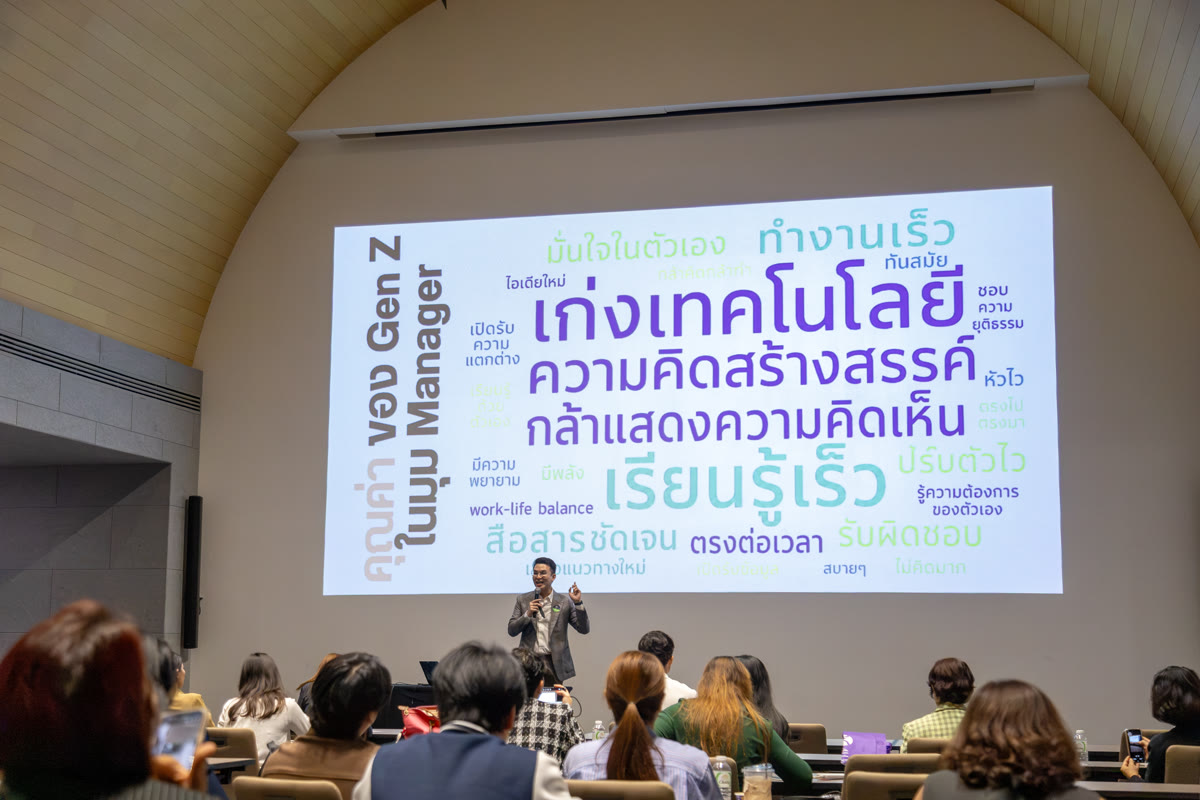 อาจารย์ภูมิพูดบนเวทีหน้าจอ ผู้ฟังนั่งหันหลังอยู่ด้านหน้า
